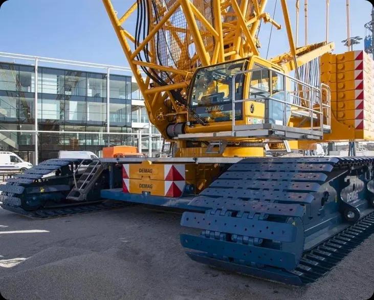 Гусеничный кран Demag жёлтого цвета на строительной площадке с зданиями в фоне