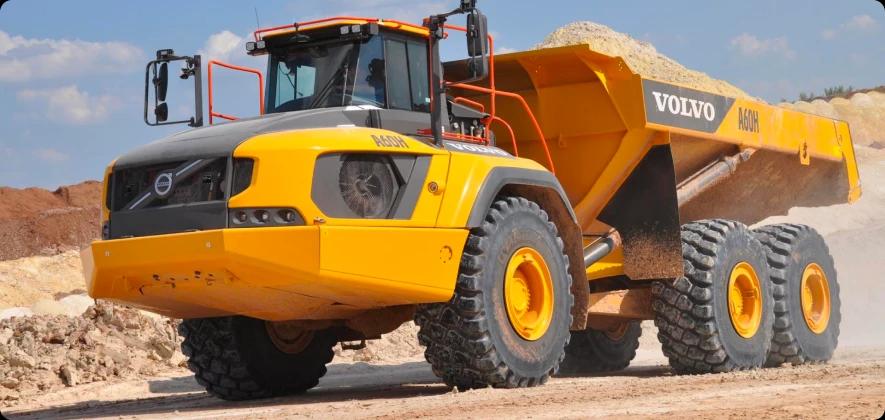 Желтый самосвал Volvo A60H едет по грунтовой дороге в гористой местности