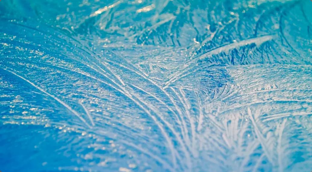 Макросъемка ледяных кристаллов с узорами на синем фоне.