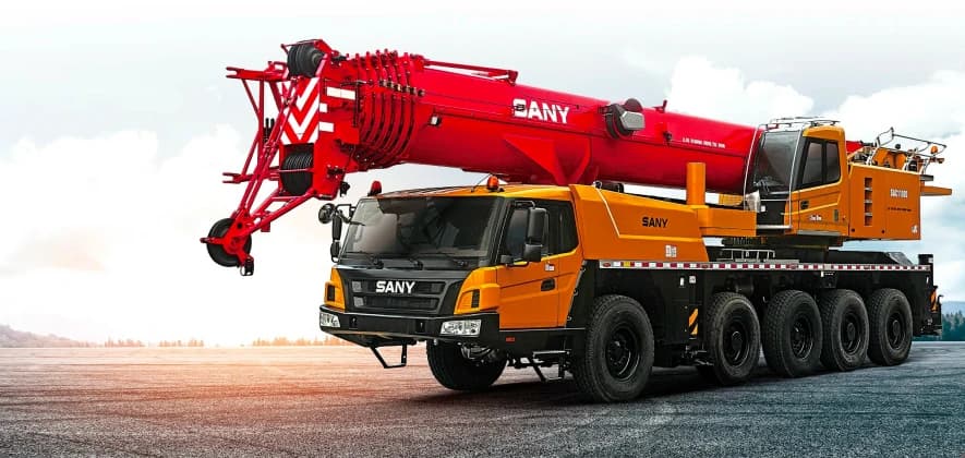 Красный и желтый самоходный кран Sany SAC1100S1, используемый для транспортировки грузов на строительной площадке